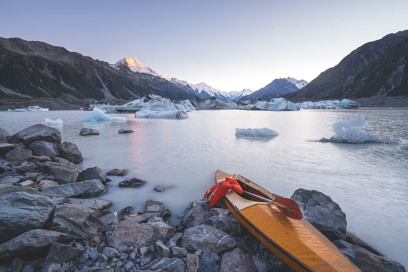 Kayak on the shores of Tasman Lake with Mount Cook in the background at sunrise