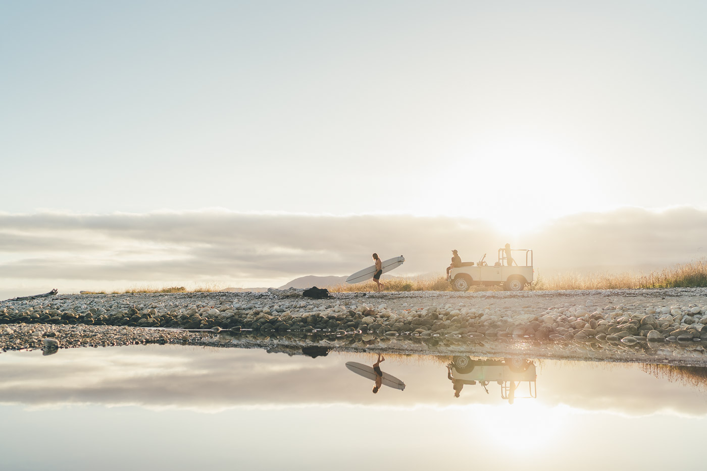 Reflection of Surfer carrying Surfboard from land Rover to the beach in New Zealand