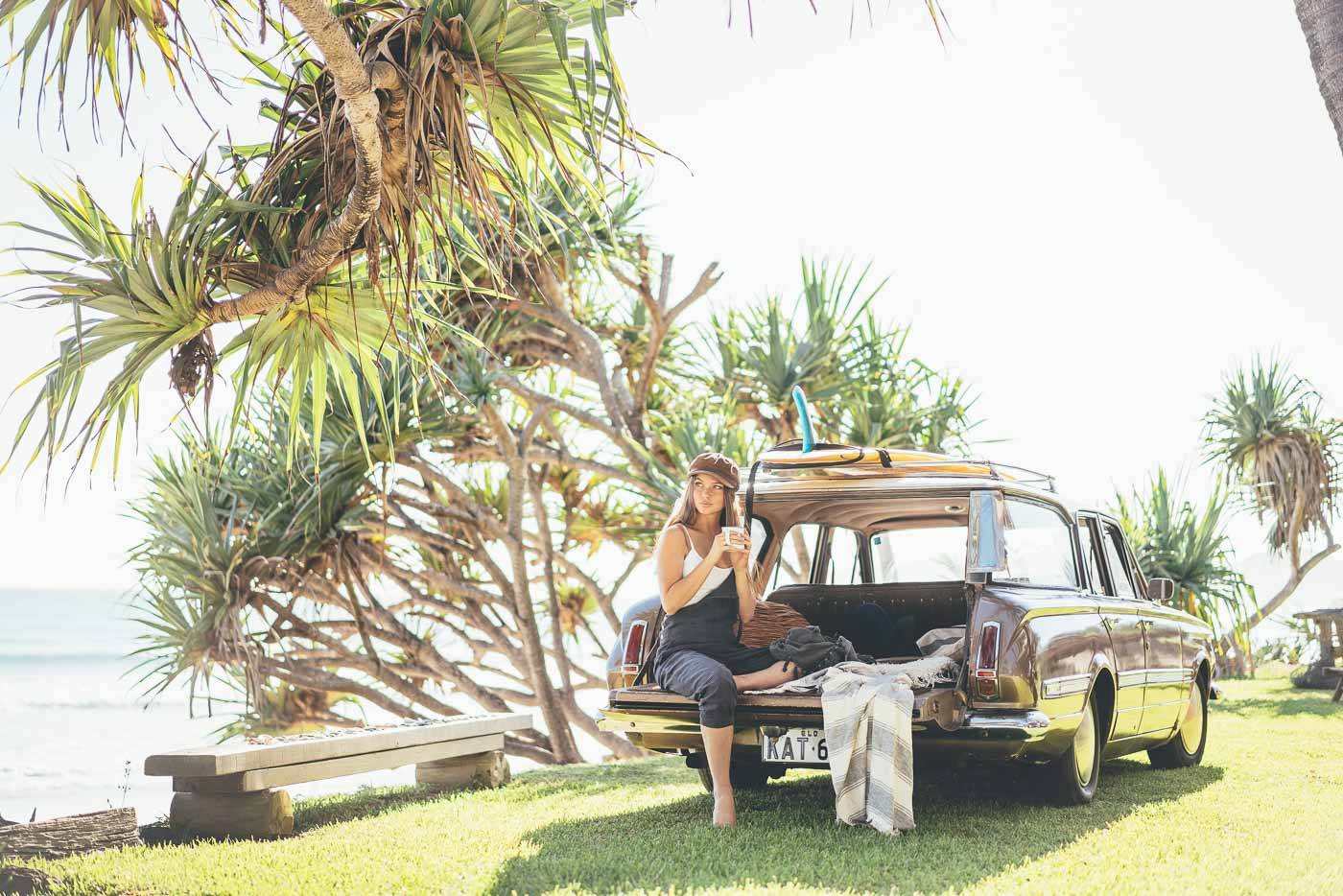 Girl sitting on the boot of the vintage car drinking coffee