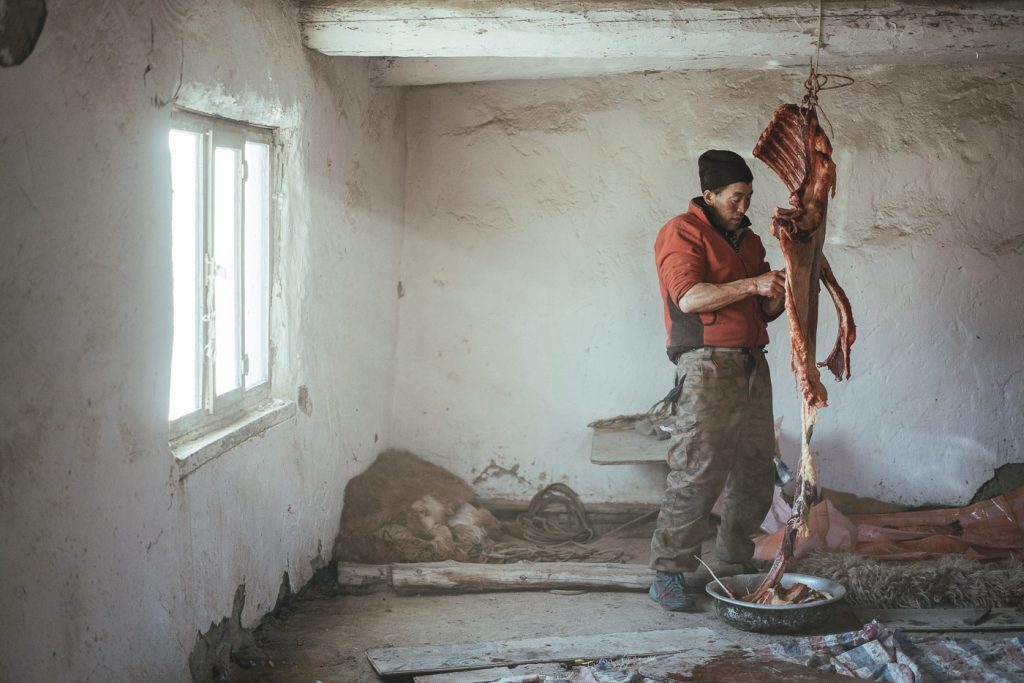 Mongolian farmer cutting meat for the winter slaughter in the storage room in Mongolia. Captured by adventure photographer Stefan Haworth