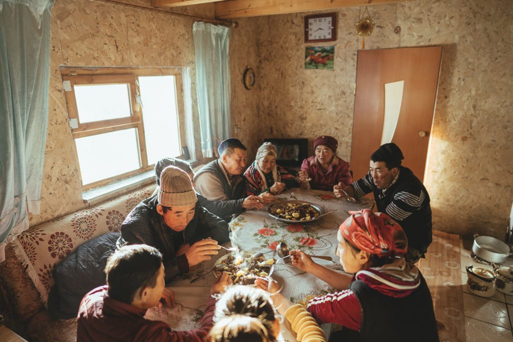 A Mongolian family eating lunch around the table in their home. Captured by Adventure photographer Stefan Haworth