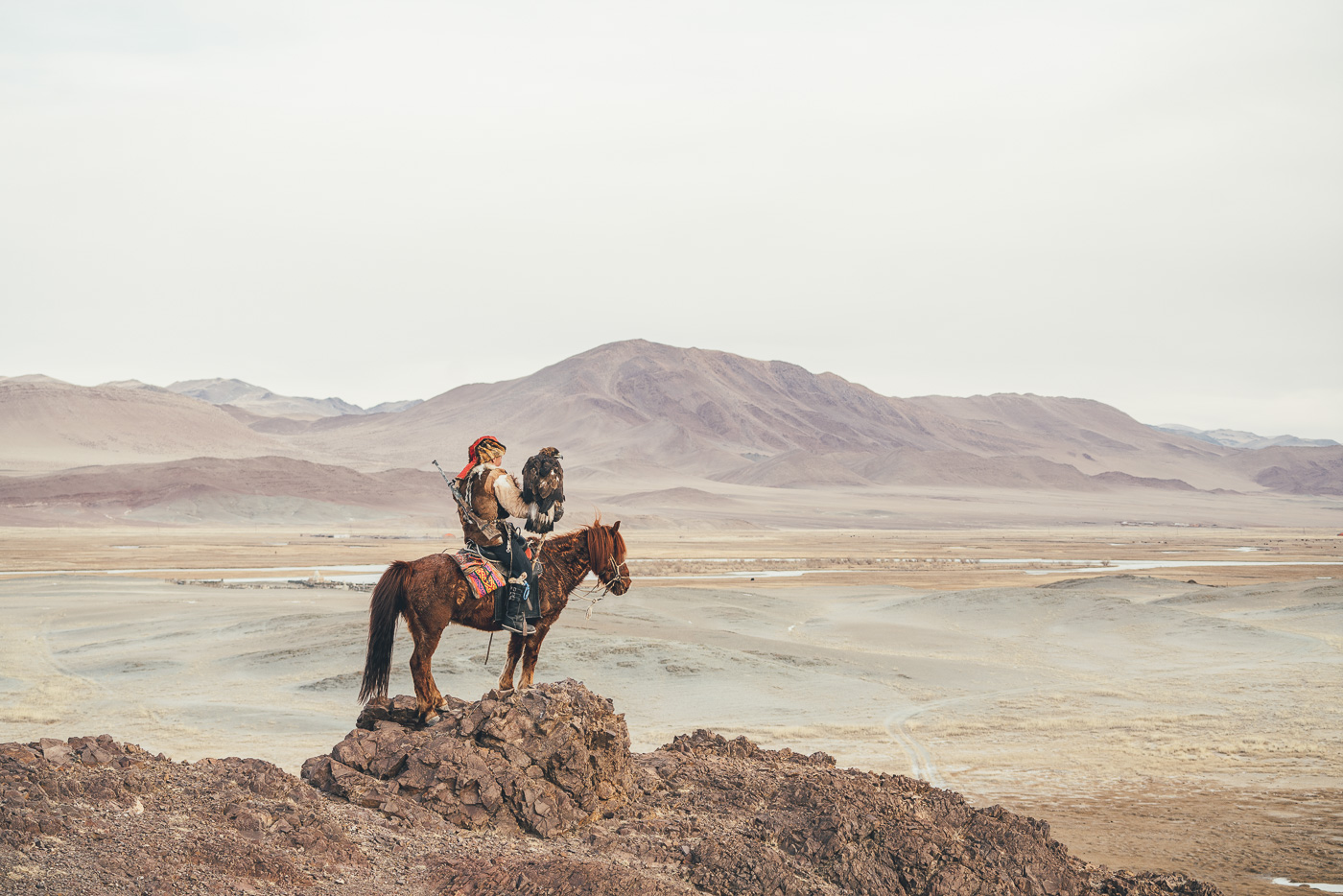 Kazakh Eagle hunter on horseback with gun on the back on top of a mountain hunting in Mongolia. Captured by adventure photographer Stefan and Haworth