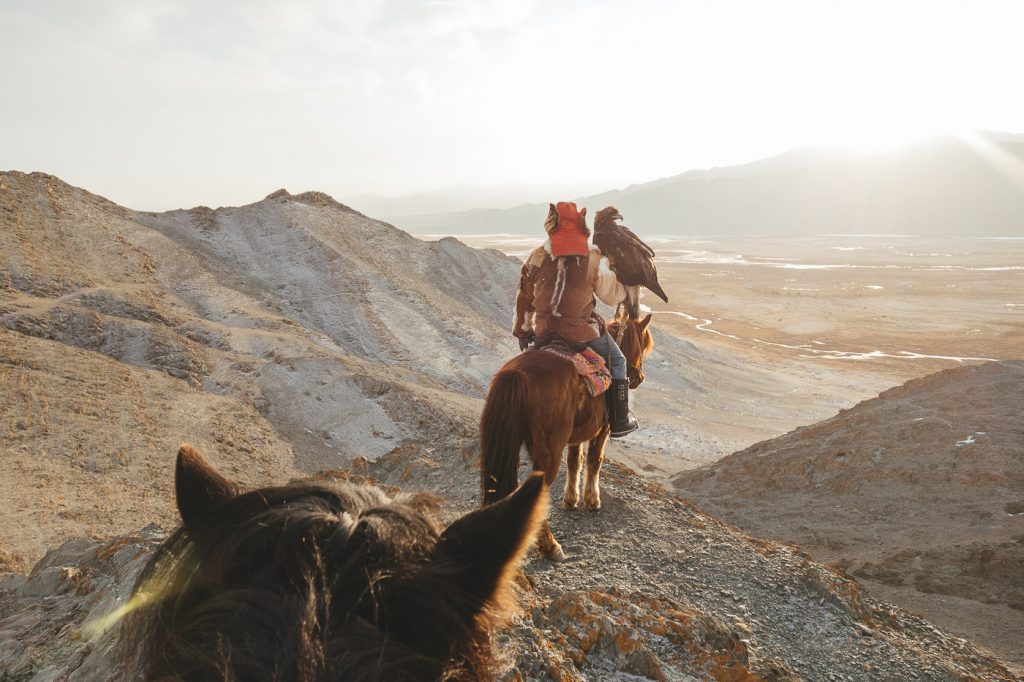 Kazakh eagle hunter on horseback looking over the valley with eagle and hand during sunset. Photographed by adventure photographer Stefan Haworth