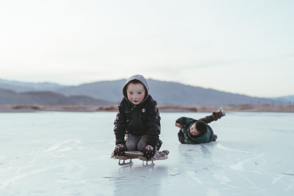 Mongolian kids playing on their home-made ice skates across the frozen river. Captured by adventure photographer stefan Haworth