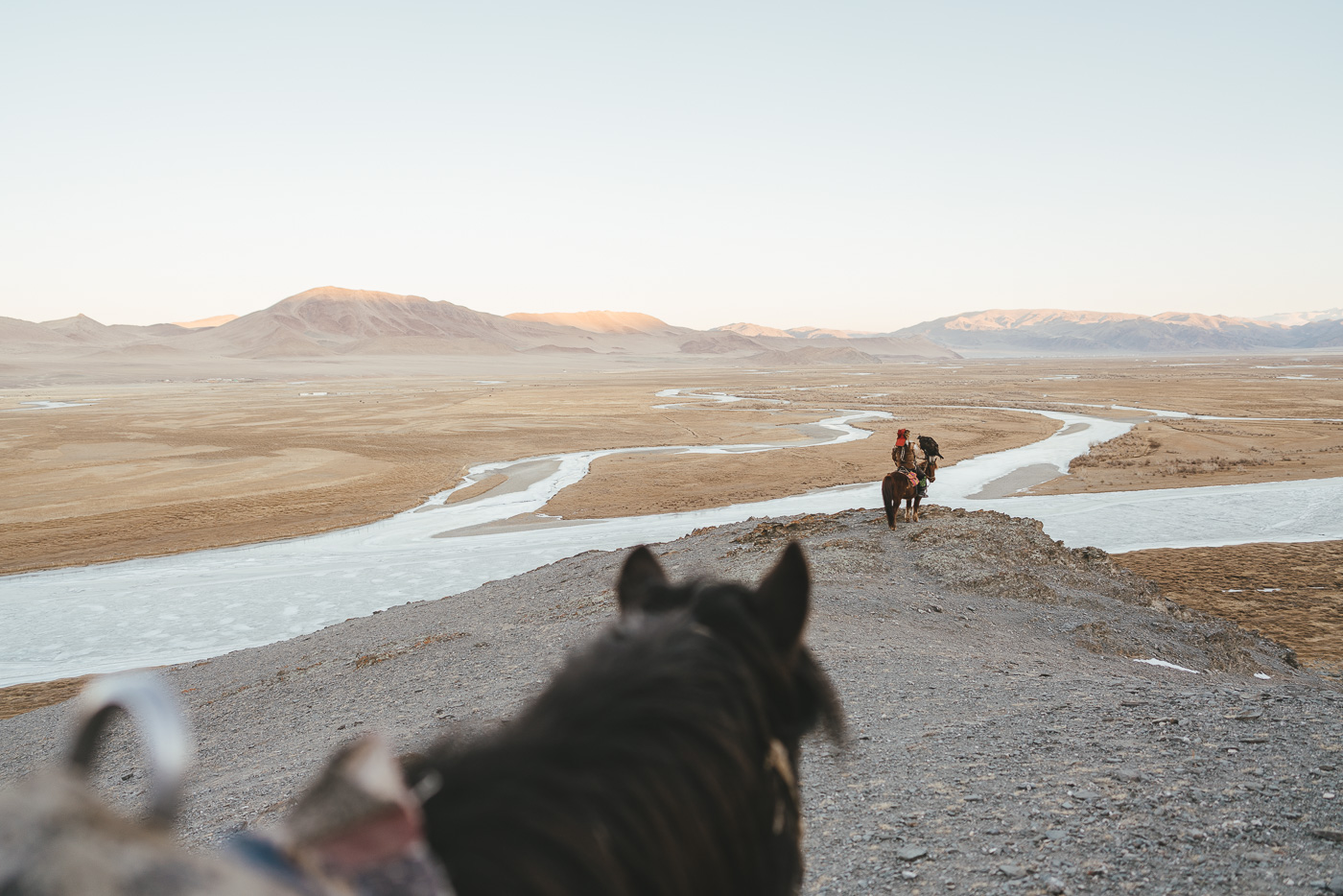 Kazakh eagle hunter on horseback looking over the frozen rivers in the valley with eagle and hand during sunset. Photographed by adventure photographer Stefan Haworth