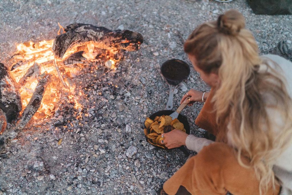 Jade Barclay cooking nachoes in a cast iron pan on the fire at Jackson bay on the west Coast of New Zealand. Captured by Sony Ambassador and Photographer Stefan Haworth