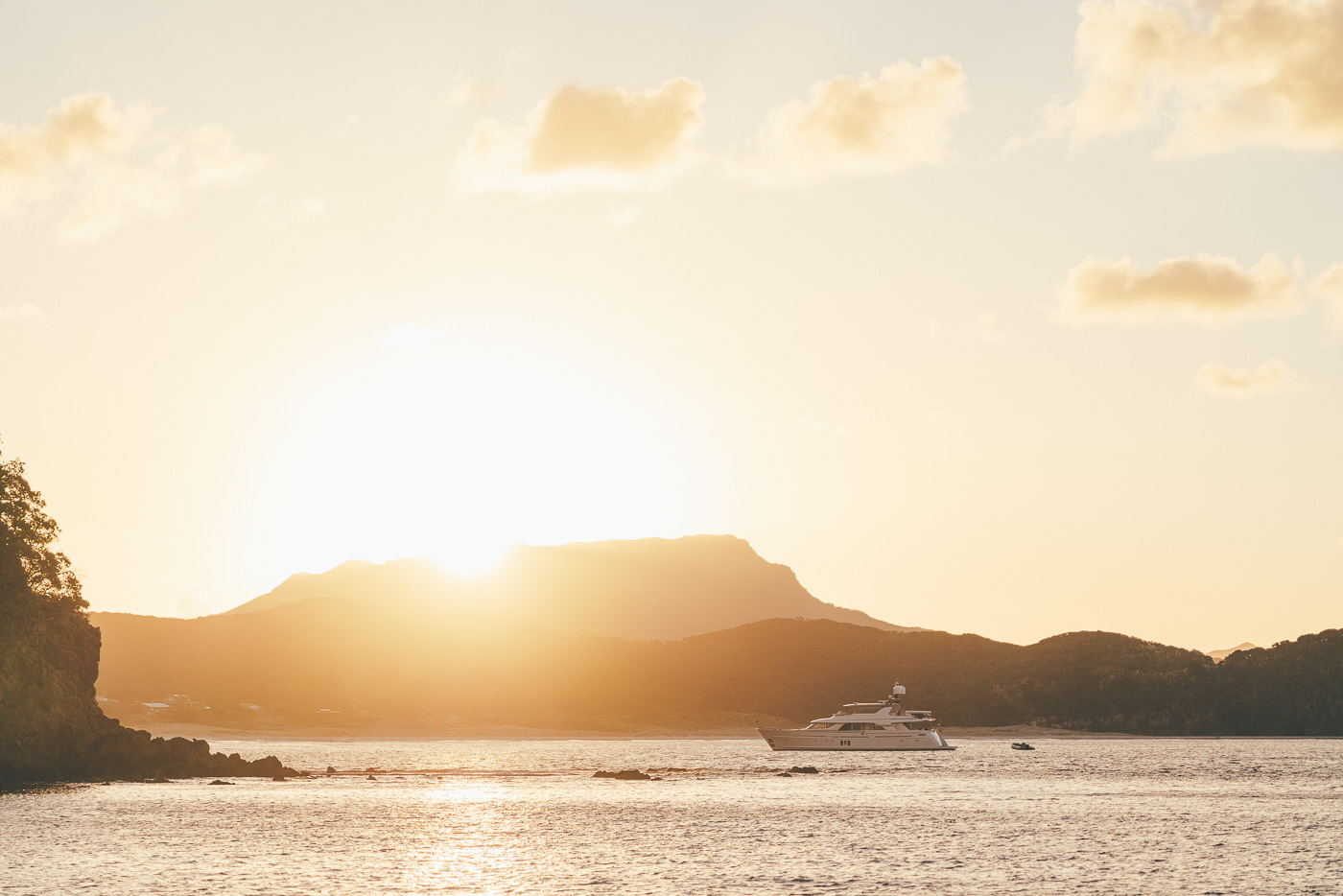 Sun setting over the hills and a yacht in the bay on Great Barrier Island. Captured by Photographer Stefan Haworth