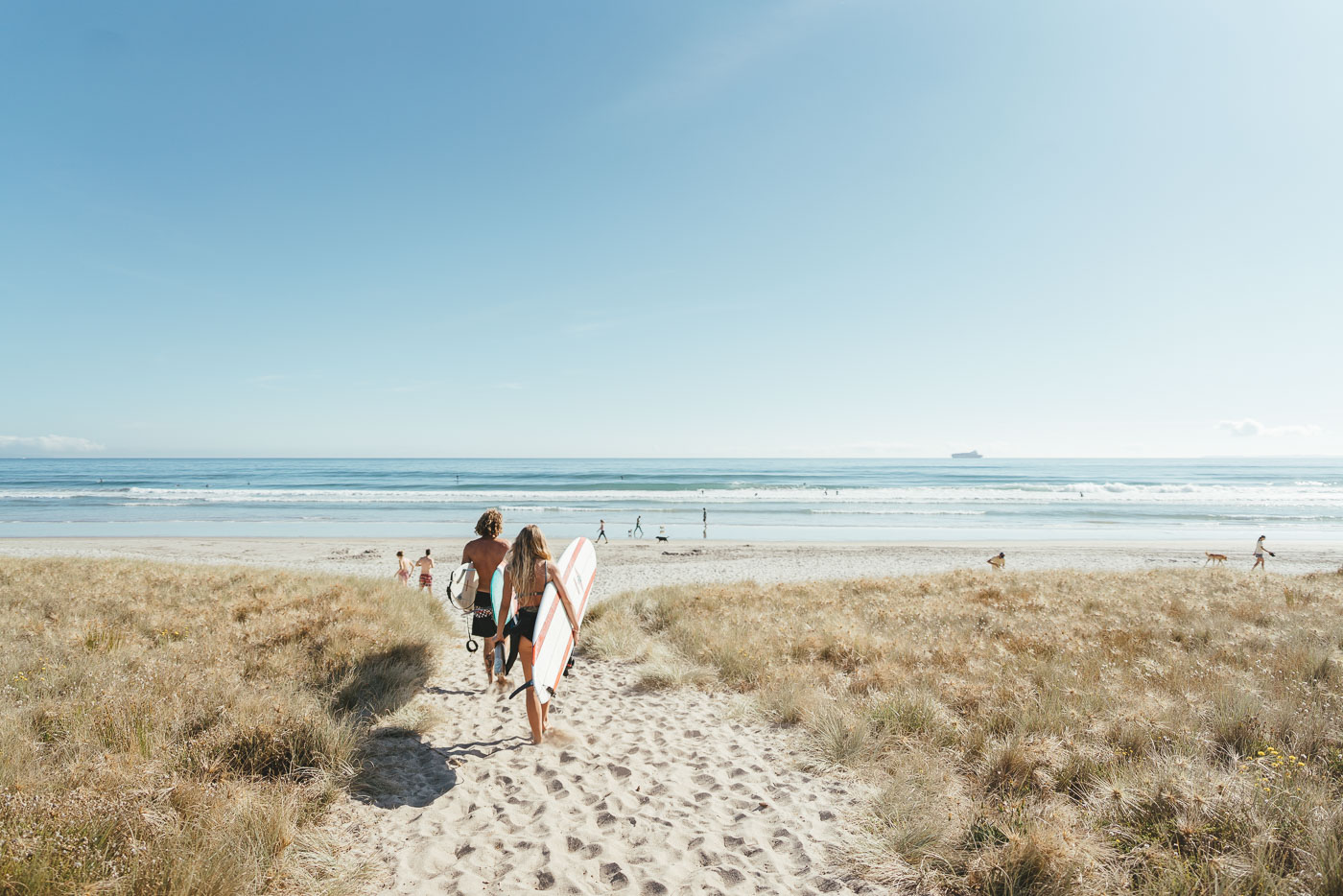 Fletch and Jade Barclay walking down the beach with Surfboard in hand at Mount Maunganui