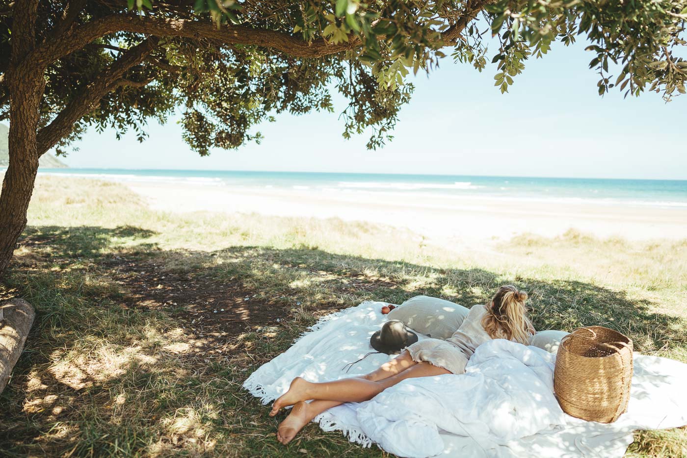 Jade Barclay under a Pohutukawa tree hiding in the shade from the sun on the beach at wainui during an East Cape Roadtrip of New Zealand. Captured by Photographer Stefan Haworth