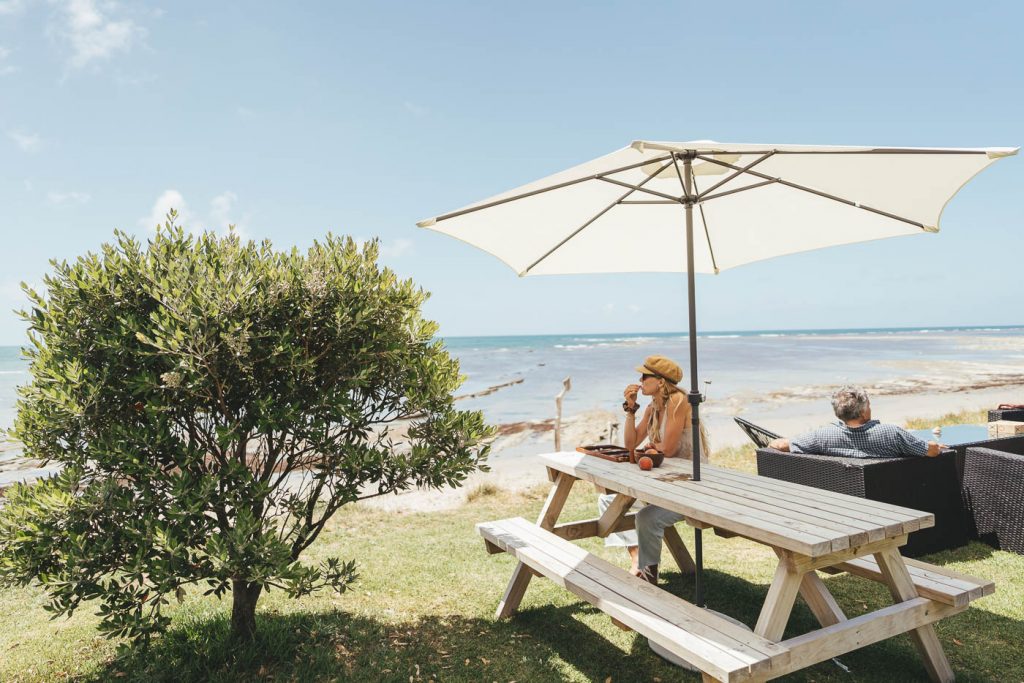 Jade Barclay eating strawberries at the Tatapouri beach under an umbrella overlooking the Ocean on the East Cape road trip of New Zealand. Captured by Stefan Haworth