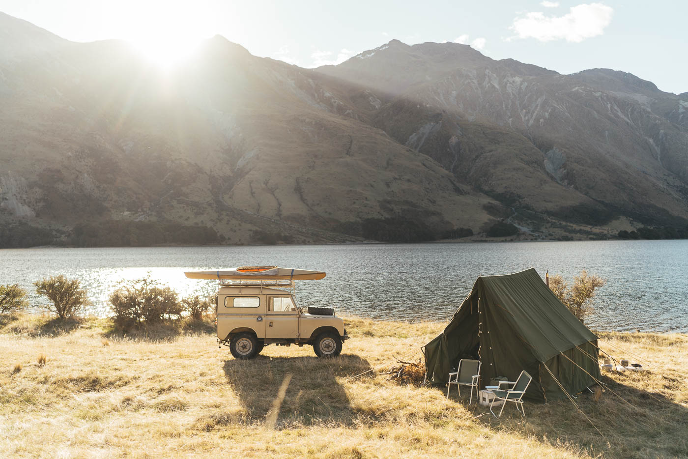 Series Land rover with a vintage kayak on the roof and Canvas tent beside a remote lake in the Southern Alps camping in New Zealand