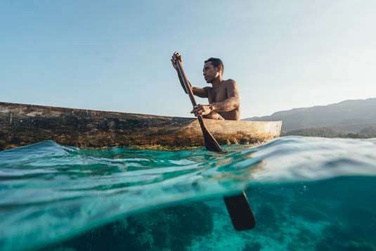 Fisherman of East Timor paddling wooden canoe out over the reef