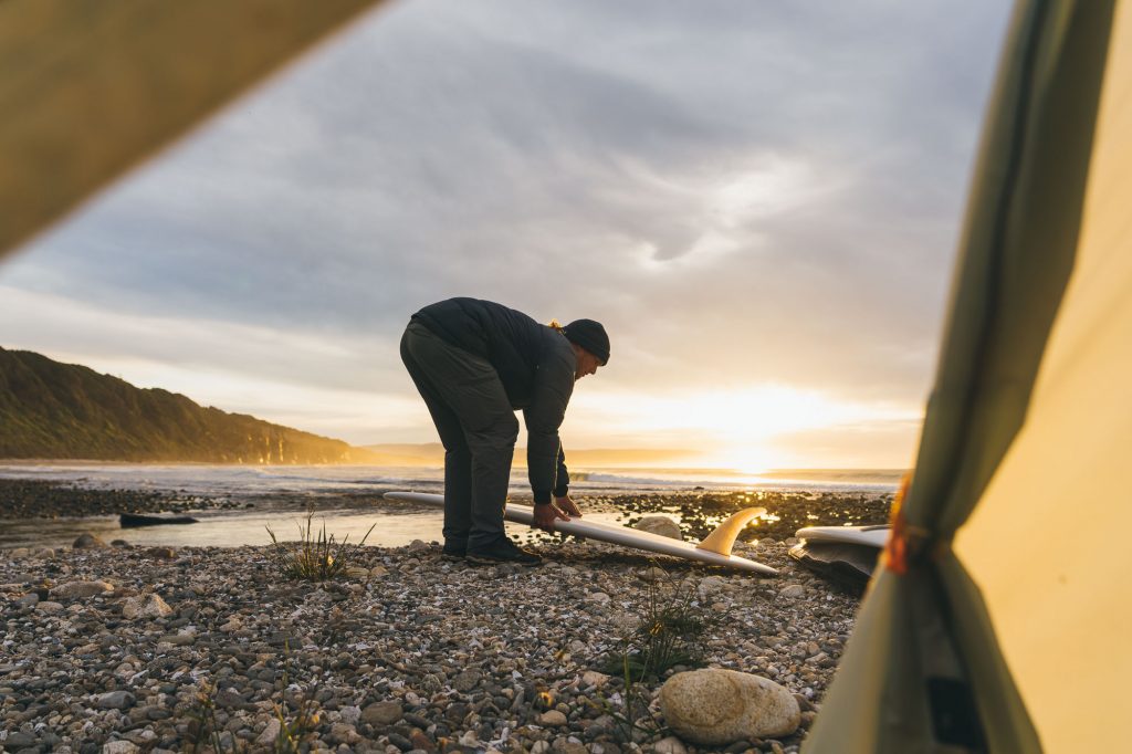 Surfer picking up surfboard while camping in South Island of New Zealand