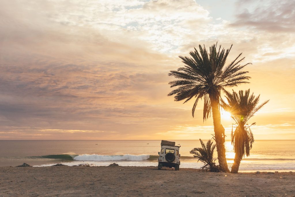 Land Rover defender parks at a famous Moroccan surf break at sunset with waves in the background