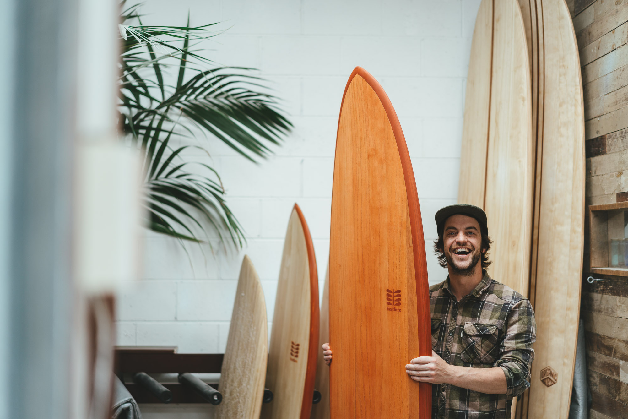 Boardshaper Jack at the verdure surfboard workshop holding a wooden mid length surfboard, Wellington