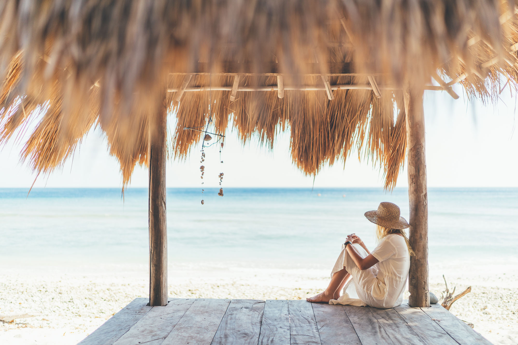 Chick sitting under a thatched roof beach cabana overlooking the ocean in East Timor