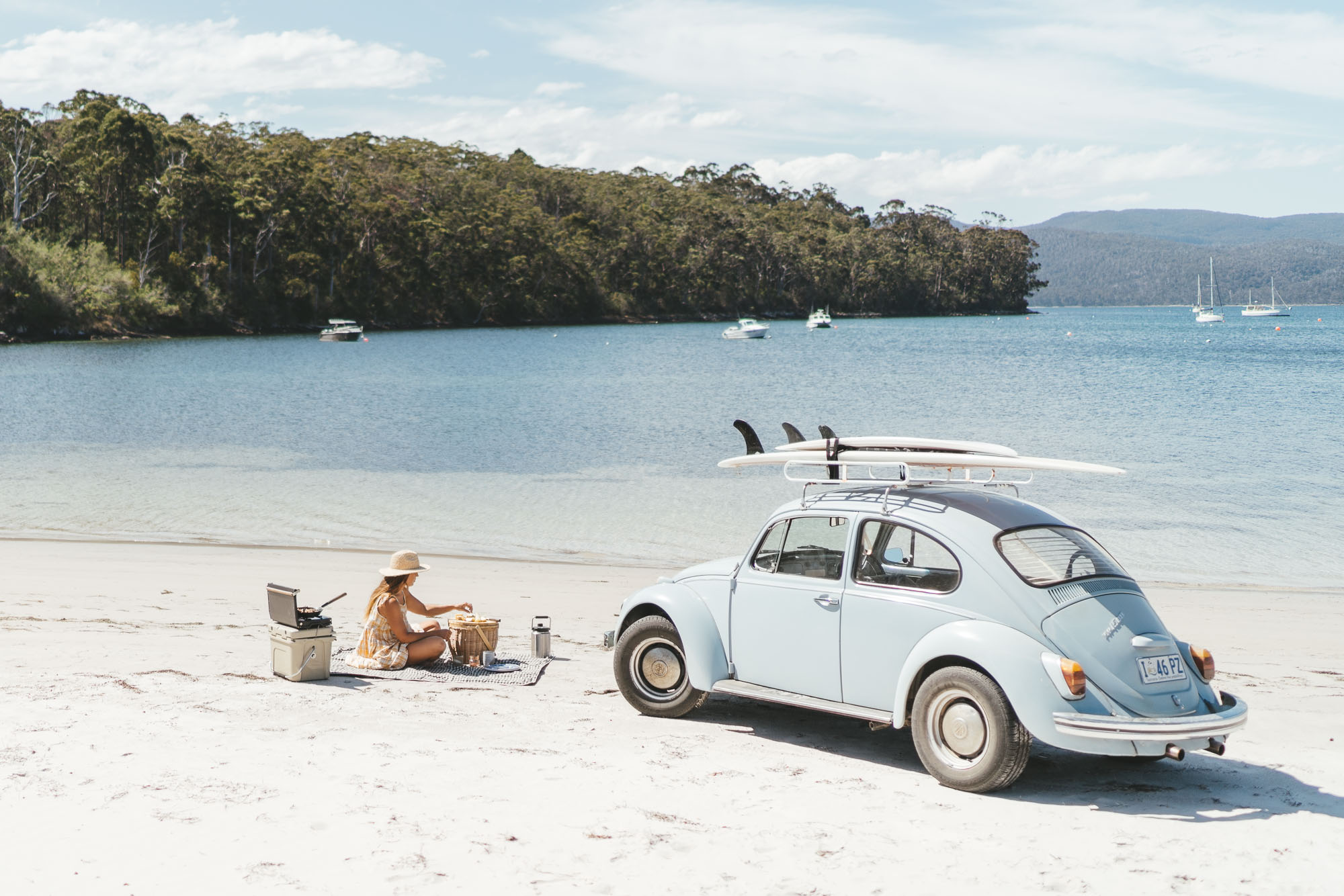 Sarah Glover cooking on the beach next to her Beetle in Tasmania, Australia.