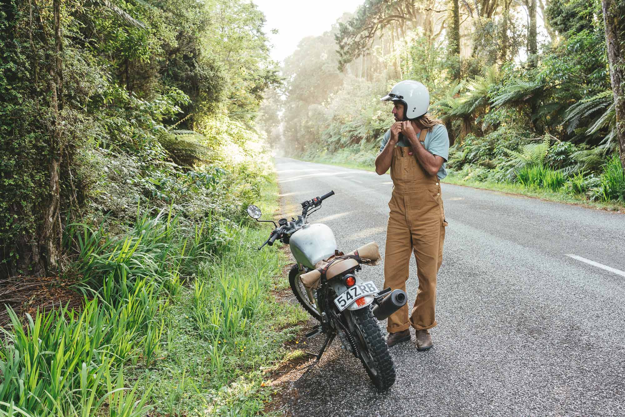 Motorbike rider doing up helmet on the Rain forest roads of the West Coast of New Zealand