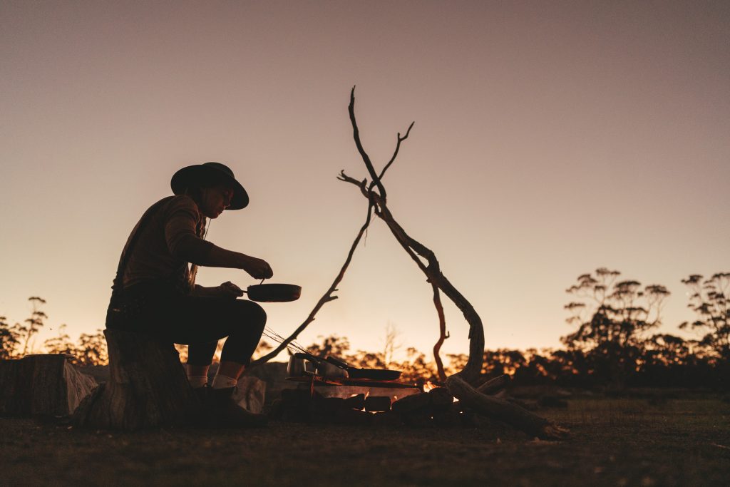 Silhouette of outdoor chef cooking over the fire at sunset in Tasmania